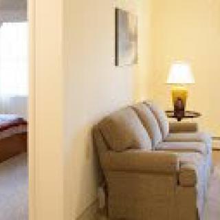 A cozy living room with a sofa and lamp, adjacent to a bedroom.