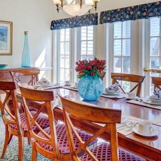 A well-lit dining room featuring a wooden table, elegant chairs, and a decorative vase with flowers.