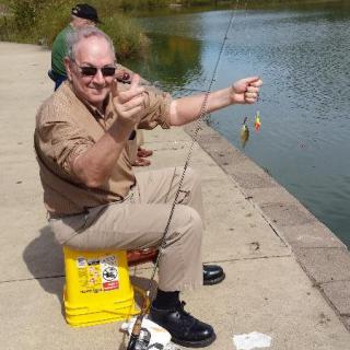 A man excitedly shows off a small catch while fishing by a lake.