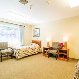 A well-lit bedroom with cozy furnishings including a bed, chairs, and lamps.
