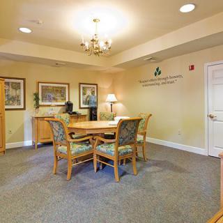 A well-lit office space featuring a wooden table with four chairs, a chandelier, and framed artwork on the walls.