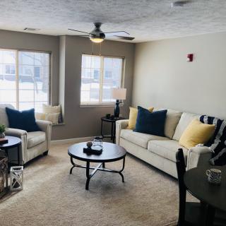 A cozy living room with neutral tones, featuring a sofa and armchairs, centered around a round coffee table.