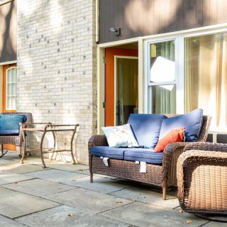 A cozy patio with wicker furniture and blue cushions, bathed in sunlight.
