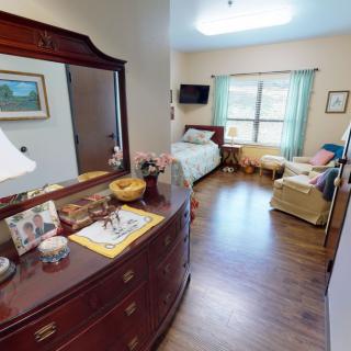 A cozy bedroom featuring a bed, a comfortable chair, and a dresser with decorative items.