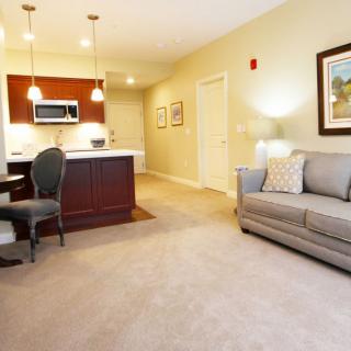 A modern living room with an integrated kitchen and dining area, featuring stylish furniture and warm lighting.