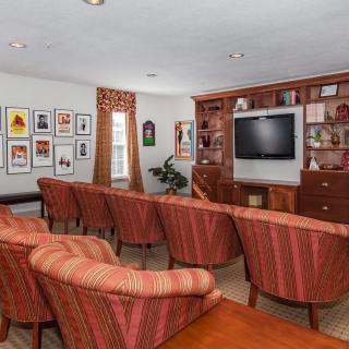 A cozy living room with striped armchairs facing a television, surrounded by bookshelves and artwork.