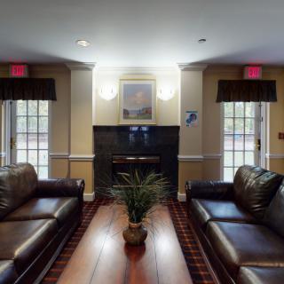 A cozy living room with leather sofas, a wooden coffee table, and a central fireplace flanked by large windows.