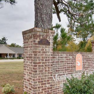 A brick sign with a plaque and tree, situated near a building surrounded by greenery.