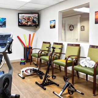 A waiting area with exercise equipment and seating, featuring a TV and decorative wall art.