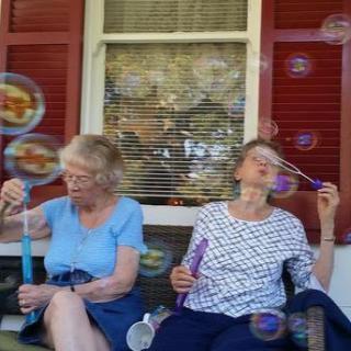 Two women blowing bubbles while sitting on a porch.