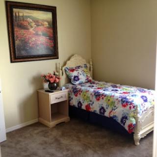 A cozy and colorful bedroom featuring a single bed with floral bedding, complemented by a nightstand and wall art.