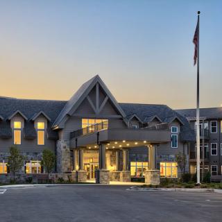 A modern building with an illuminated entrance and a flagpole at dusk.