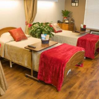 A cozy hospital or nursing home room with two beds, adorned with red blankets and warm decor.