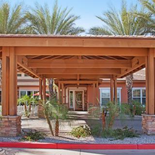A building entrance with a wooden pergola surrounded by desert landscaping and palm trees.