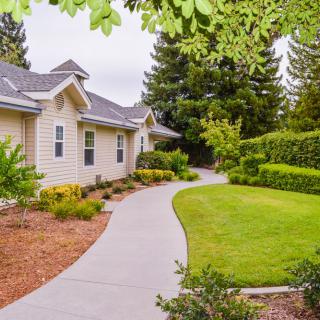 A peaceful residential property with a well-maintained lawn and garden, featuring a curved pathway leading to the house.