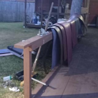 Several mats are draped over a fence in an outdoor yard area during the evening.