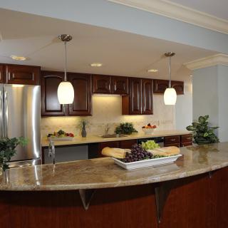 A modern kitchen featuring wood cabinets, marble countertops, and stainless steel appliances with pendant lighting.