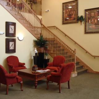 A cozy lobby area featuring red armchairs, a wooden coffee table, and decorative artwork near a staircase.