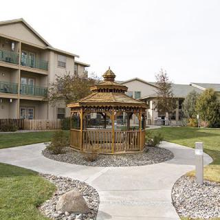 A charming wooden gazebo surrounded by a manicured garden pathway and adjacent buildings.