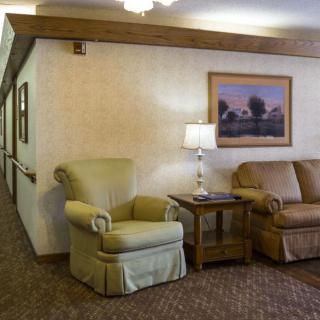 A cozy living room with an armchair, sofa, and a lamp on a side table, featuring wall artwork.