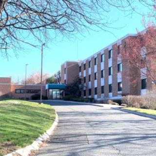 A multi-story brick building with a driveway and surrounding trees.