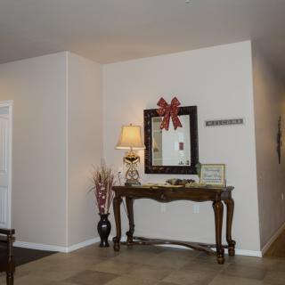 A cozy living room corner featuring a decorative table with a mirror above, adorned with a bow, and accompanied by a lamp and flower vase.