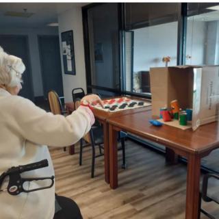 An elderly woman engaging in an activity at a table with blocks and a checkerboard.