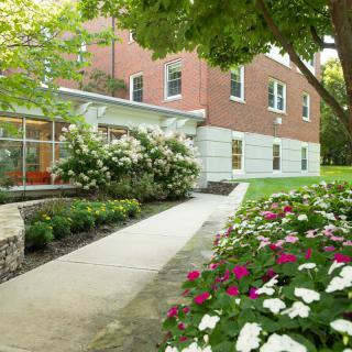 A scenic view of a building with a pathway surrounded by lush greenery and colorful flowers.