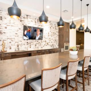 A modern dining area with a long bar counter, pendant lighting, and a brick accent wall featuring a mounted television.
