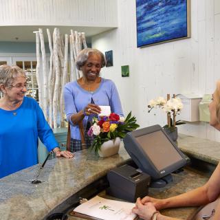 Two elderly women smiling at a receptionist while checking in with a card.