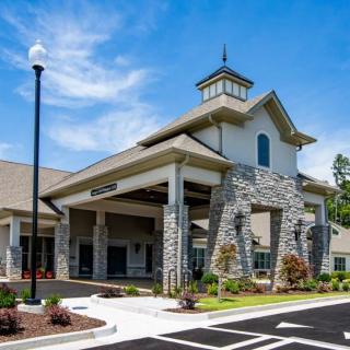 A modern building with a stone facade and landscaped entrance under a clear blue sky.