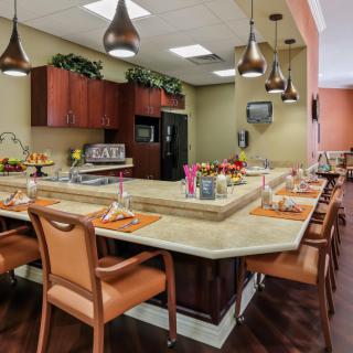 A modern kitchen and dining area featuring a large countertop surrounded by chairs and illuminated by pendant lights.