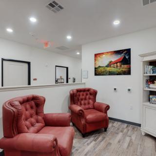 A cozy waiting room with two red armchairs and a colorful artwork on the wall.