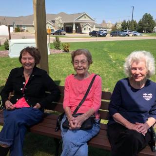 Three people sitting on a bench enjoying a sunny day in the park.