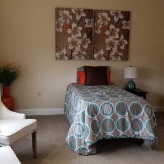 A cozy bedroom with a single bed, decorated with a patterned comforter and floral wall art.