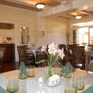 A well-lit dining room with an elegantly set table featuring flowers and glasses.