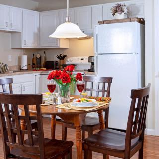 A cozy kitchen with a dining table set for a meal, featuring red flowers and wine glasses.