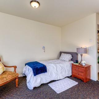 A cozy bedroom with a single bed, nightstand, lamp, and armchair.