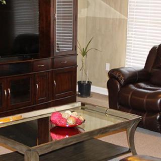 A cozy living room featuring a leather chair, a glass-top coffee table, and an entertainment center with a television.
