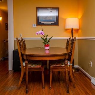 A cozy dining room with a wooden table and four chairs, decorated with an orchid centerpiece, and illuminated by a floor lamp against a yellow wall.