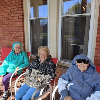 Three elderly individuals sitting on chairs outside a brick building, enjoying a sunny day.