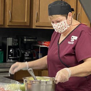 A chef wearing a mask and gloves preparing food in a kitchen.