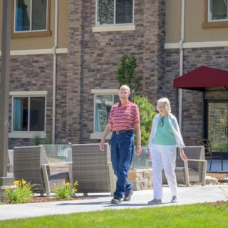 An elderly couple walking together in the garden of a retirement home.