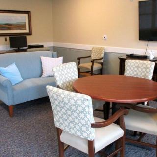 A cozy living area featuring a sofa, round wooden table, comfortable chairs, and a wall-mounted TV.