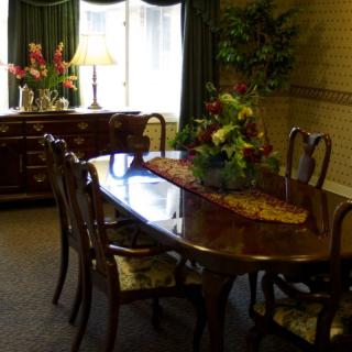 A classic dining room setup with a polished wooden table, elegant chairs, floral centerpiece, and soft lighting.