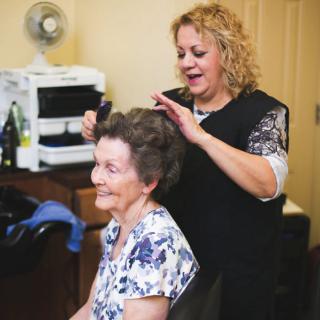 A hair stylist is happily working on an elderly woman's hair in a salon.