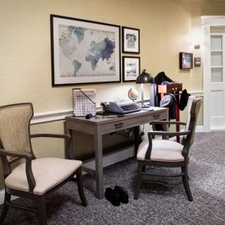 A cozy office space with a desk and two chairs, featuring wall art and soft lighting.