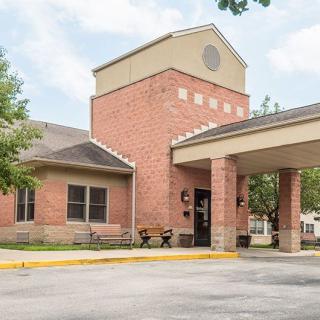 A brick building with a covered entrance and benches outside, surrounded by trees.