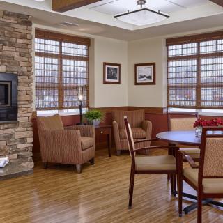 A cozy living room with a fireplace, chairs, wooden floor, and decorative artwork on the walls.