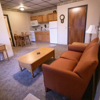 A cozy apartment interior featuring a living room with a sofa and a coffee table, adjacent to a small kitchen and dining area.